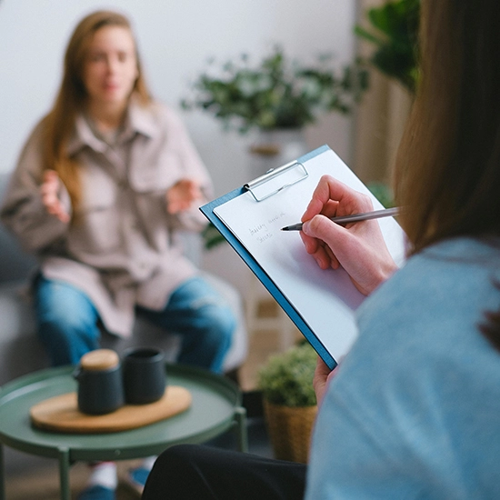 Un coach professionnel prenant des notes sur un bloc-notes pendant une séance avec un client en arrière-plan