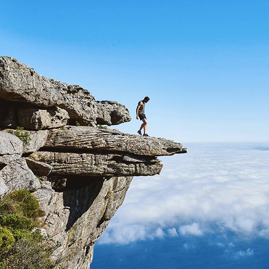 Un randonneur debout au bord d'une falaise surélevée, avec un paysage de nuages en contrebas donnant l'illusion d'une mer de nuages sous un ciel bleu clair